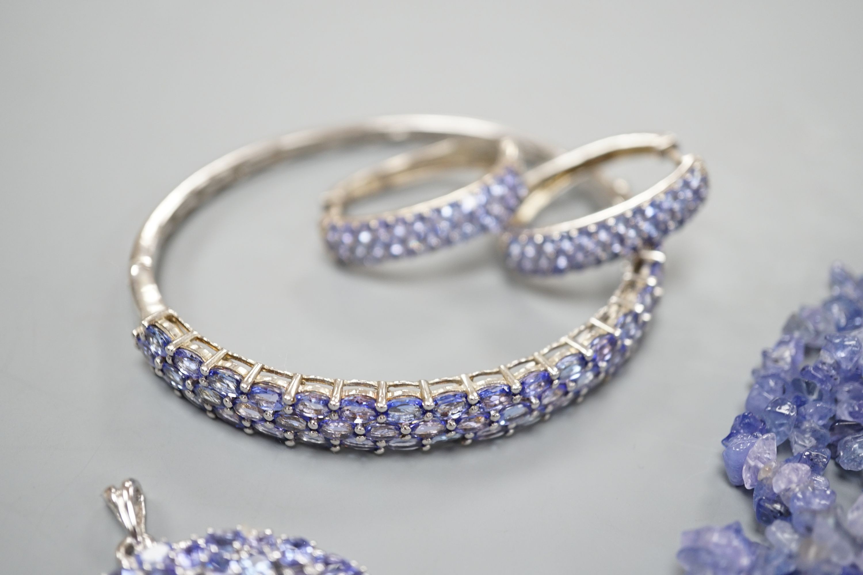 A modern 925 and tanzanite set hinged bangle, a similar pair of earrings and pendant and a rough cut tanzanite set necklace.
